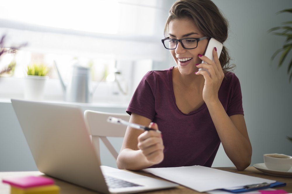 uma mulher falando ao celular enquanto usa um laptop