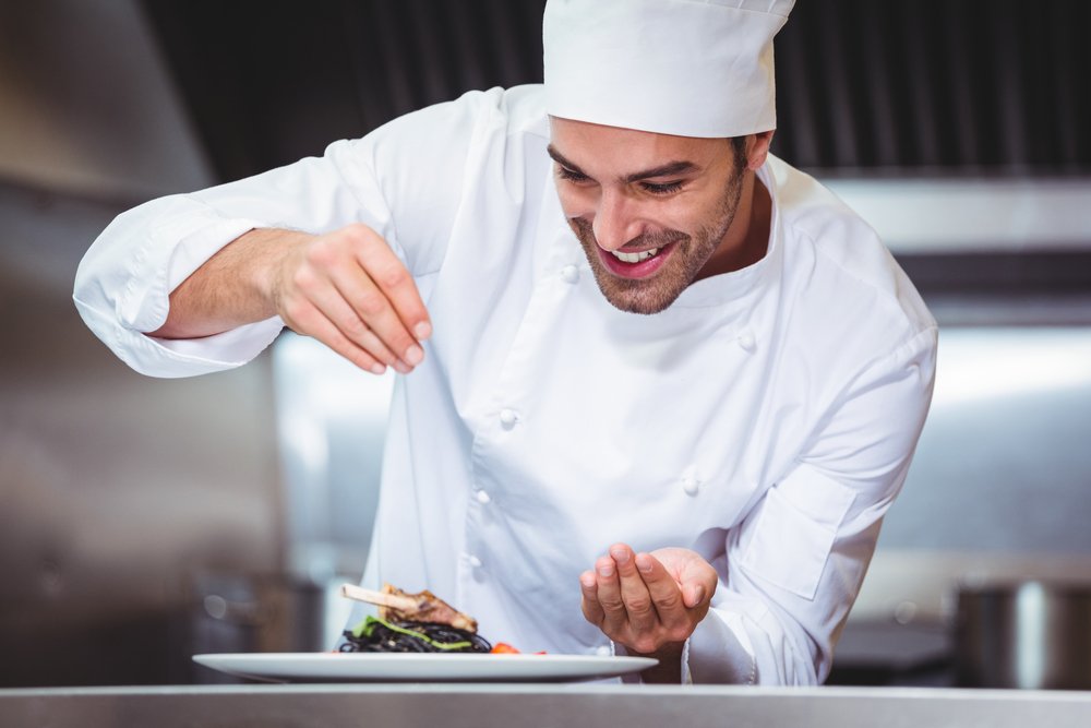 um homem com chapéu de chef está preparando comida em um prato