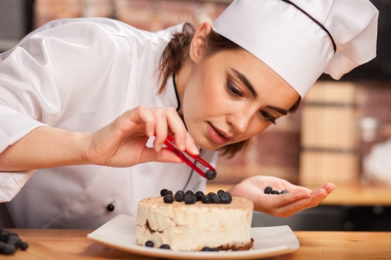 uma mulher com chapéu de chef decorando um bolo