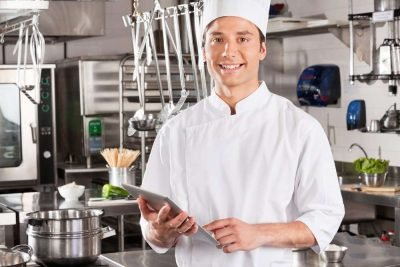 um homem com chapéu de chef segurando um tablet em uma cozinha