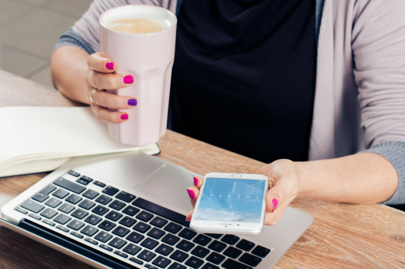 uma mulher sentada à mesa com uma xícara de café e um telefone celular