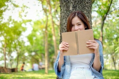 uma mulher sentada debaixo de uma árvore segurando um caderno