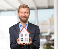 Gestor de negócios imobiliários segurando uma casa em miniatura, simbolizando gestão de imóveis e negócios no setor imobiliário, em ambiente empresarial