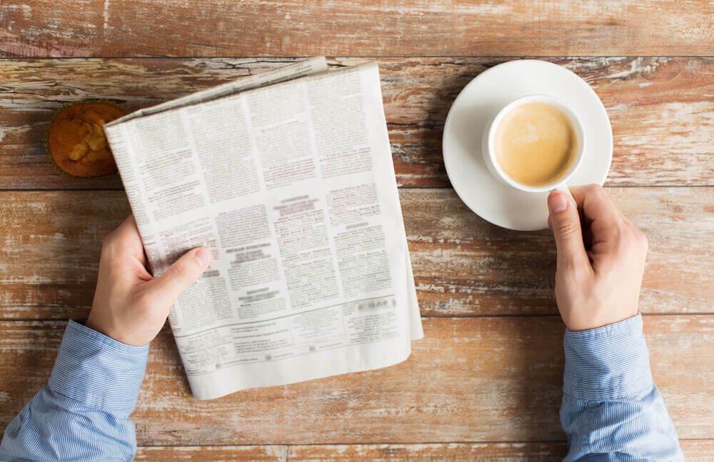 uma pessoa lendo um jornal ao lado de uma xícara de café