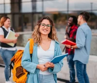 Estudantes felizes interagindo ao ar livre, com materiais escolares como cadernos e mochilas coloridas. Um ambiente universitário vibrante e colaborativo.