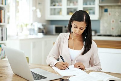 uma mulher sentada à mesa da cozinha escrevendo em um pedaço de papel