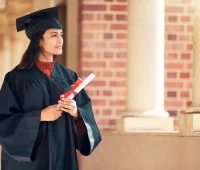 Mulher em trajes de formatura segurando diploma, olhando para o horizonte. A imagem representa a celebração da conquista acadêmica e realizações.