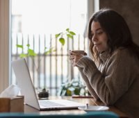 Mulher em casa, sentada, tomando café em frente ao computador