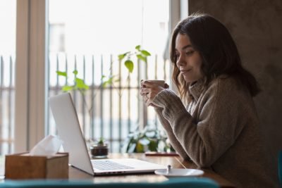 Mulher em casa, sentada, tomando café em frente ao computador