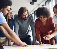 Grupo diverso de pessoas colaborando em atividades de brainstorming com notas adesivas coloridas em uma mesa, promovendo trabalho em equipe e criatividade.
