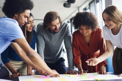 Grupo diverso de pessoas colaborando em atividades de brainstorming com notas adesivas coloridas em uma mesa, promovendo trabalho em equipe e criatividade.