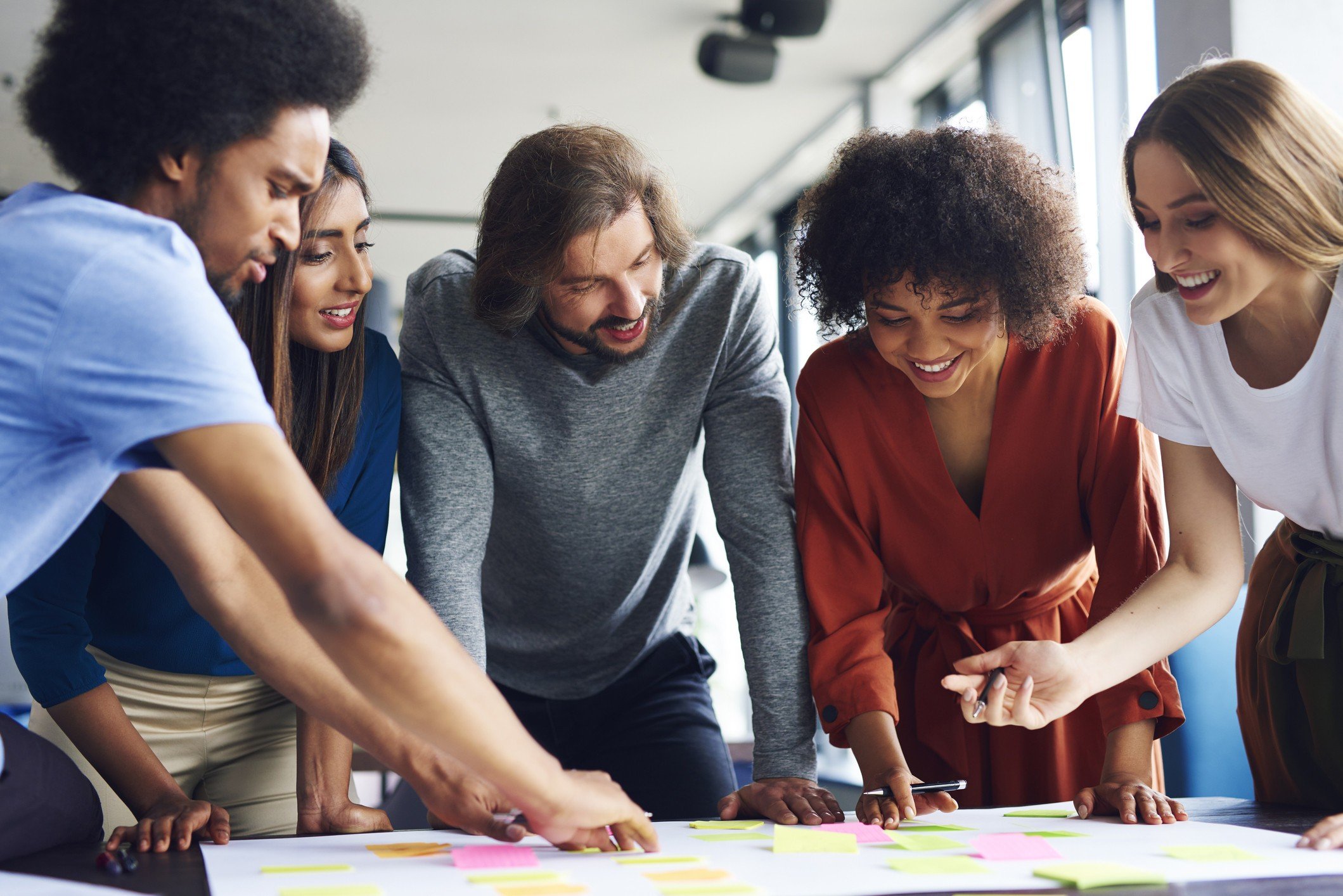Grupo diverso de pessoas colaborando em atividades de brainstorming com notas adesivas coloridas em uma mesa, promovendo trabalho em equipe e criatividade.