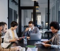 Grupo de profissionais colaborando em uma reunião de negócios com laptops e materiais de trabalho em uma sala moderna.