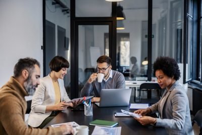 Grupo de profissionais colaborando em uma reunião de negócios com laptops e materiais de trabalho em uma sala moderna.
