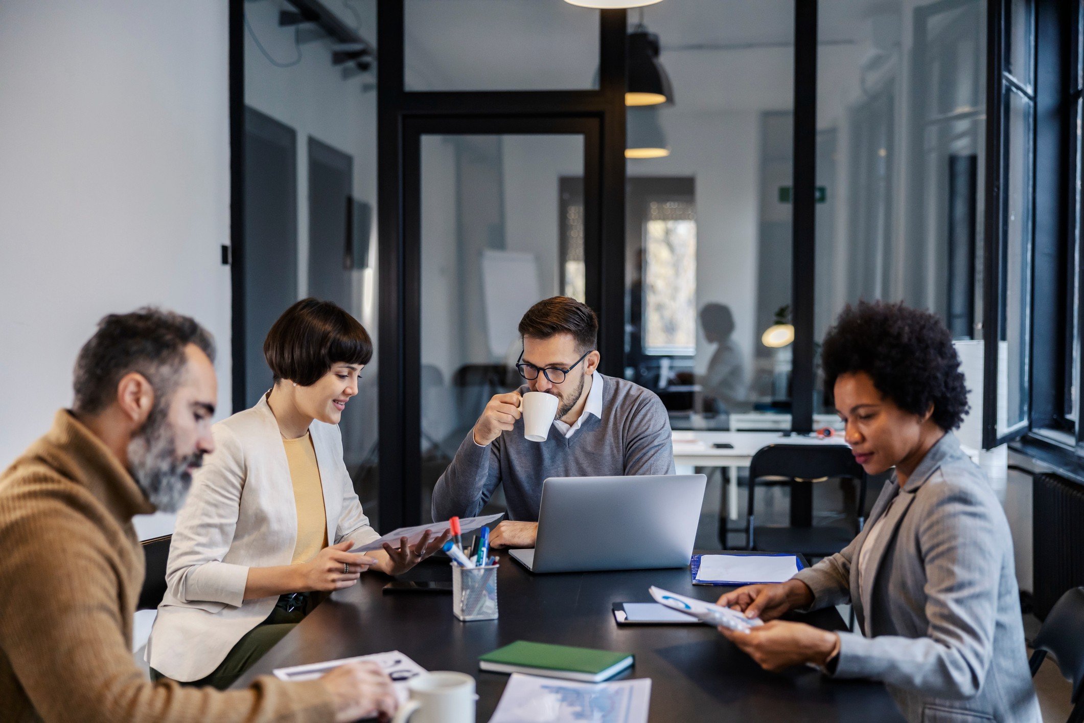 Grupo de profissionais colaborando em uma reunião de negócios com laptops e materiais de trabalho em uma sala moderna.