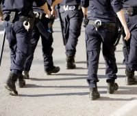 Imagem de policiais em uniforme, caminhando em direção ao alvo. A cena demonstra a atuação das forças de segurança pública em um ambiente urbano.