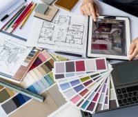 Imagem de um projeto de design de interiores com amostras de cores, papel de croqui, lápis de cor e um tablet exibindo um ambiente decorado.