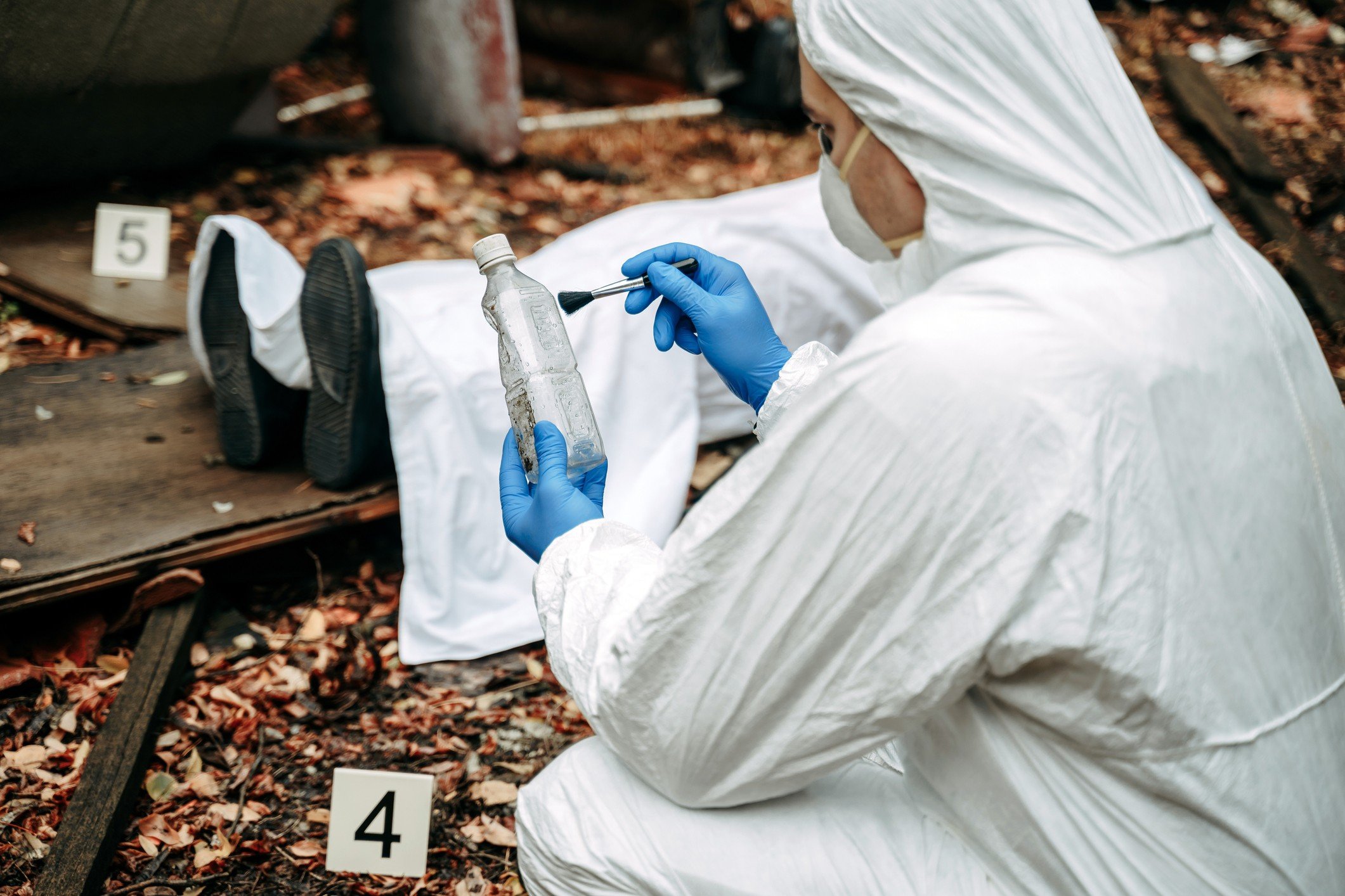 Profissional forense analisando evidências em cena de crime, com botellas e objetos identificados, em um cenário misterioso.