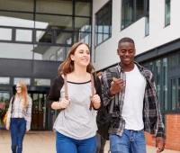 Grupo de estudantes caminhando em direção à entrada de uma instituição de ensino, demonstrando uma atmosfera de camaradagem e felicidade.