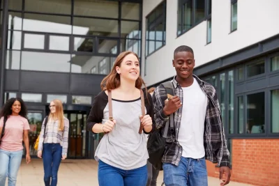 Grupo de estudantes caminhando em direção à entrada de uma instituição de ensino, demonstrando uma atmosfera de camaradagem e felicidade.