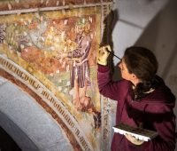 Artista restaurando uma pintura mural antiga, destacando detalhes e técnicas de conservação, em um ambiente com luz suave.