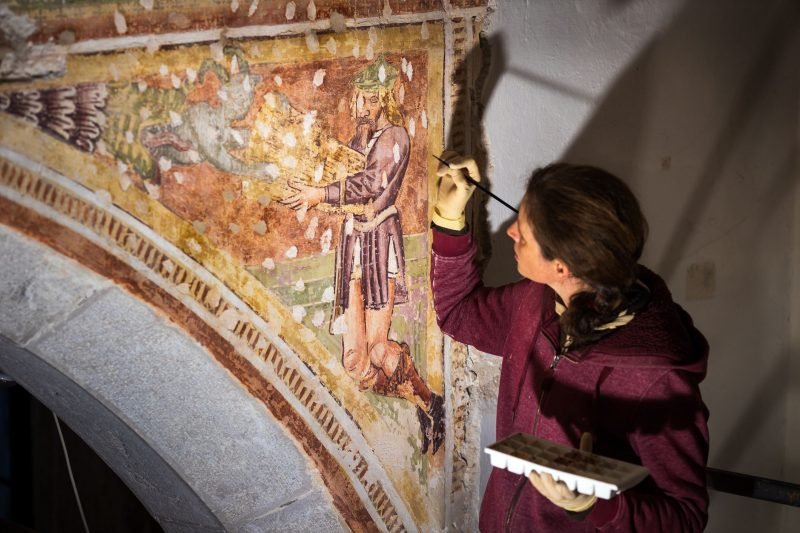 Artista restaurando uma pintura mural antiga, destacando detalhes e técnicas de conservação, em um ambiente com luz suave.