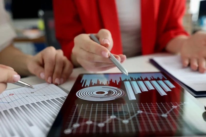 Profissionais analisando gráficos e dados em um tablet, com gráficos de barras e círculo, simbolizando finanças e análise de dados.