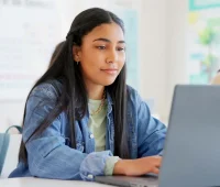 Estudante concentrada usando laptop em ambiente de aprendizado. A imagem retrata a importância da tecnologia no estudo e na educação.