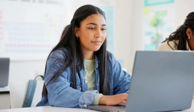 Estudante concentrada usando laptop em ambiente de aprendizado. A imagem retrata a importância da tecnologia no estudo e na educação.
