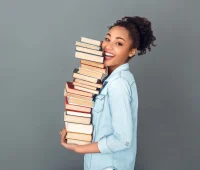 Uma jovem sorridente está segurando uma pilha de livros, transmitindo alegria e amor pela leitura. Ideal para promover a importância da educação e do saber.
