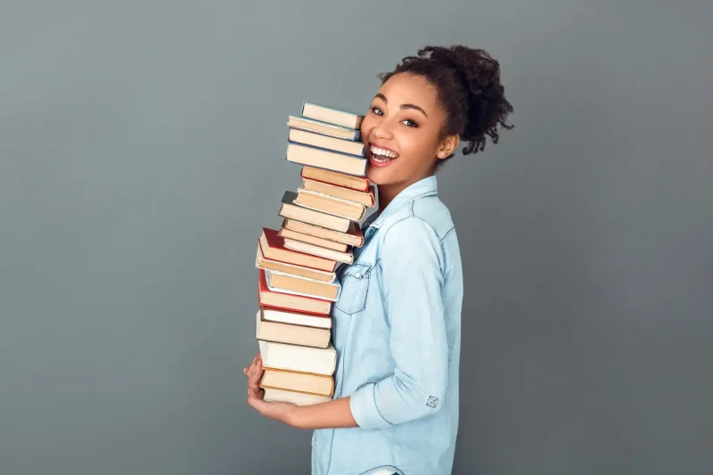 Uma jovem sorridente está segurando uma pilha de livros, transmitindo alegria e amor pela leitura. Ideal para promover a importância da educação e do saber.