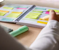 Pessoa organizando tarefas em um caderno com post-its coloridos. O planejamento é fundamental para aumentar a produtividade e o foco nas atividades.