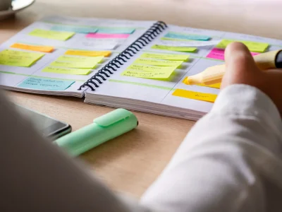 Pessoa organizando tarefas em um caderno com post-its coloridos. O planejamento é fundamental para aumentar a produtividade e o foco nas atividades.