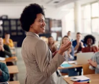 Professora sorridente interagindo com alunos em sala de aula, promovendo um ambiente de aprendizado inspirador e motivador. Alunos aplaudindo, destacando a importância da educação.