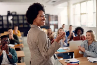 Professora sorridente interagindo com alunos em sala de aula, promovendo um ambiente de aprendizado inspirador e motivador. Alunos aplaudindo, destacando a importância da educação.
