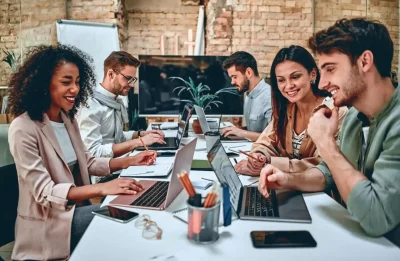 Grupo de pessoas trabalhando em equipe em um escritório moderno, usando laptops e colaborando em projetos, ilustrando o conceito de trabalho em equipe e produtividade.