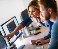 Profissionais colaborando em um ambiente de trabalho moderno, analisando dados em computadores. A imagem retrata a dinâmica de trabalho em equipe na tecnologia.
