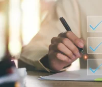 Pessoa escrevendo em uma prancheta com marcações de verificação, simbolizando a organização e o cumprimento de tarefas, representando produtividade.
