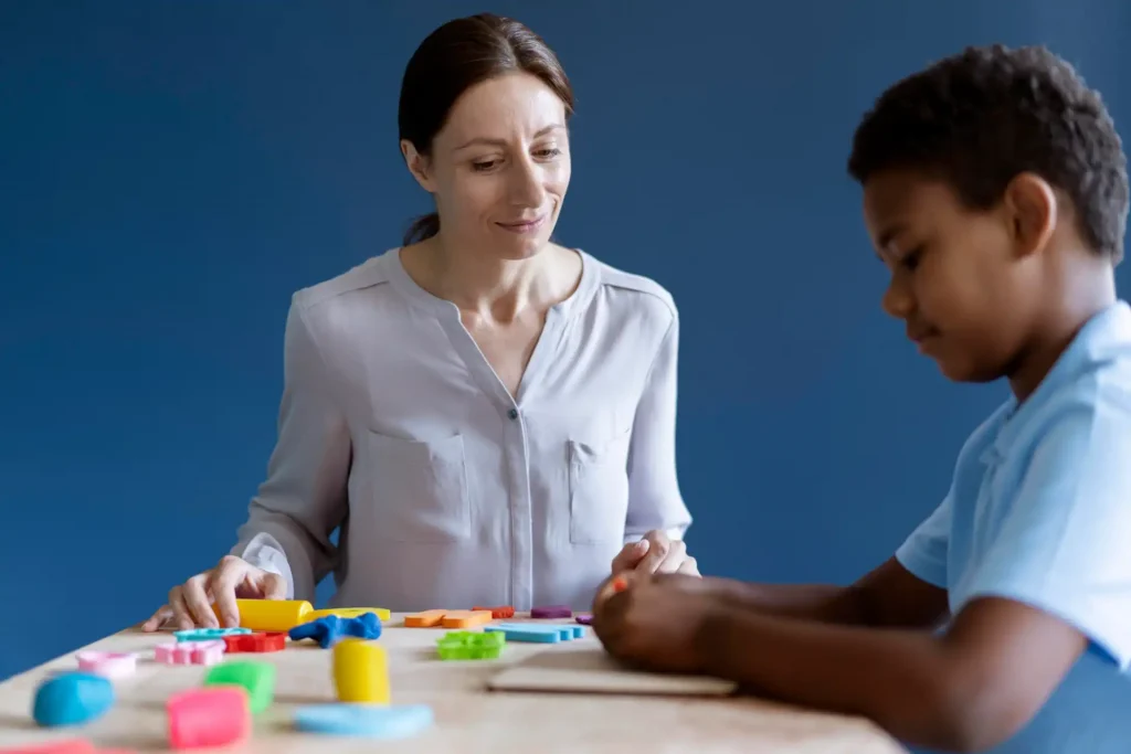 Imagem de uma professora ajudando uma criança com autismo durante uma sessão terapêutica com jogos e atividades educativas.