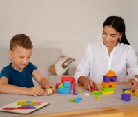 Acompanhante terapêutico auxiliando uma criança com autismo a brincar com blocos de montar coloridos, promovendo desenvolvimento e inclusão.
