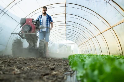 Homem cultivando hortaliças em estufa agrícola com tecnologia moderna, utilizando máquina de cultivo para melhorar a produção de alimentos em ambiente protegido