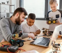 Cena escolar com crianças e um jovem mentor treinando robótica educacional, usando kits de robôs e tecnologia para aprender sobre engenharia e automação.