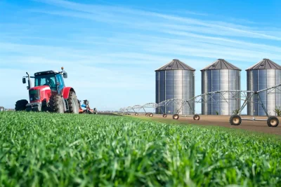 Vista de uma fazenda agrícola com trator, silos de armazenamento de grãos e sistemas de irrigação, destacando a importância da agronomia e do agronegócio no desenvolvimento rural.