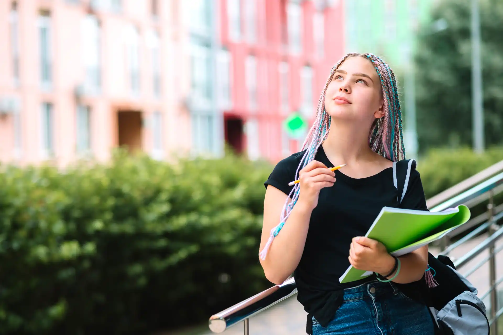 Jovem estudante universitária pensando em nota do ENEM enquanto segura caderno na mão ao ar livre, em frente a um prédio universitário.