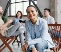 Grupo de pessoas participando de uma sessão de psicologia organizacional em um ambiente moderno e acolhedor, com foco na líder sorridente no centro.
