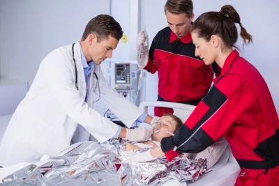 Equipe médica e de enfermagem em hospital, com profissional usando estetoscópio examinando paciente deitado e equipe ao lado ajudando no procedimento, em ambiente hospitalar.