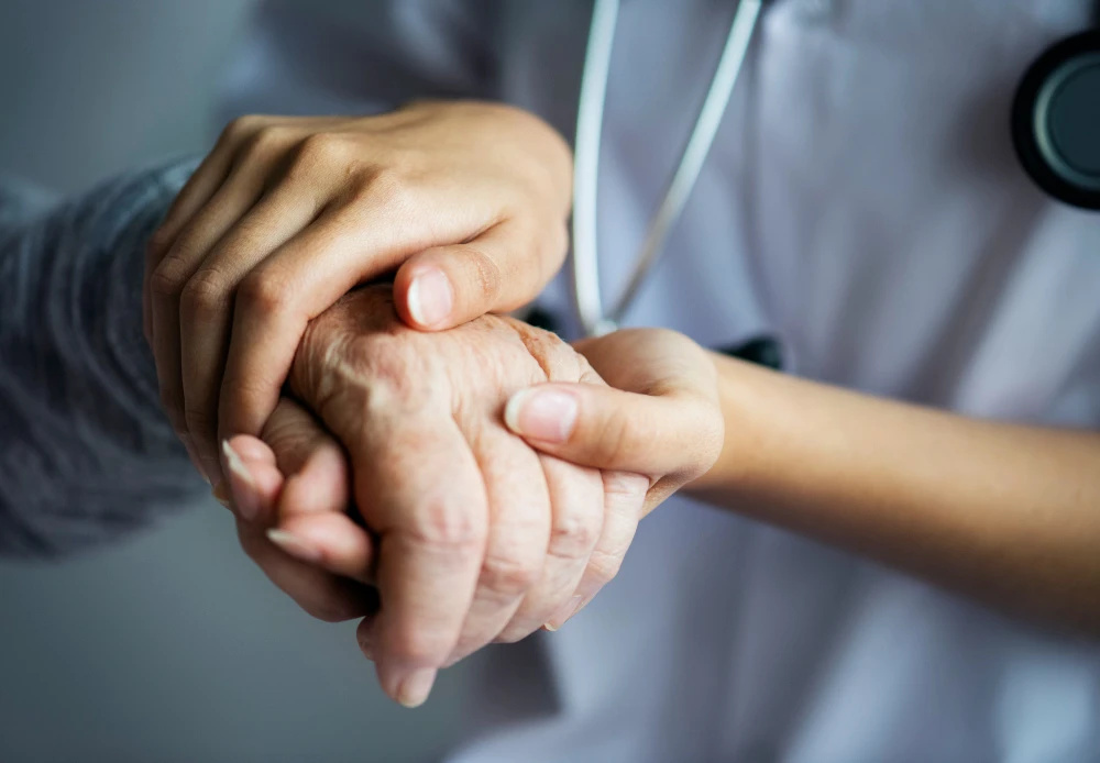 Mãos de um profissional de saúde segurando a mão de um paciente, simbolizando cuidado médico, assistência na saúde, empatia, apoio e tratamento.