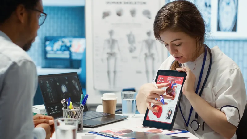 Médicos discutindo uma análise de imagem de um coração com um tablet em uma consulta médica, enfatizando tecnologia médica moderna.