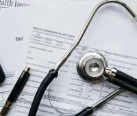 Formulário de seguro saúde com carimbo “Health Insurance Claim Form”, canetas e estetoscópio sobre uma mesa, sugerindo atendimento médico, sinistro e documentação para reembolso.