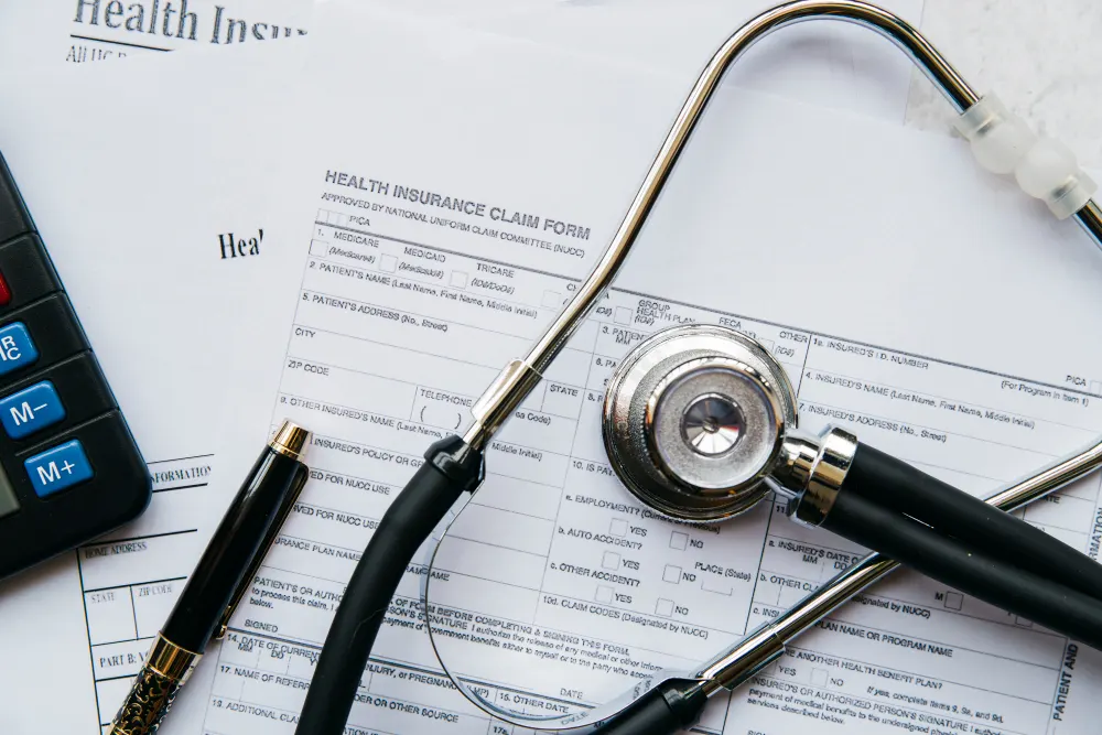 Formulário de seguro saúde com carimbo “Health Insurance Claim Form”, canetas e estetoscópio sobre uma mesa, sugerindo atendimento médico, sinistro e documentação para reembolso.